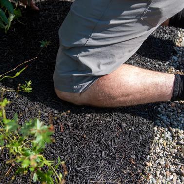 Person kneeling on Recycled Rubber Walkway at edge of garden bed and gravel surface