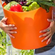 Closeup of woman's arms holding 11 Gallon Orange Tubtrug filled with freshly harvested vegetables