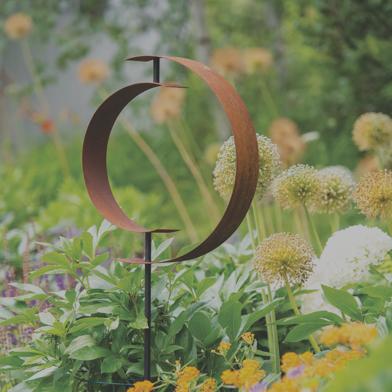 Corten Circle Garden Sculpture in garden bed of flowers
