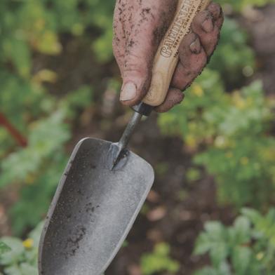 Dirt-covered hand holding Gardener's Lifetime Trowel in garden bed