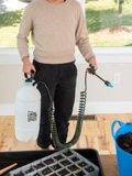 A woman holding the Indoor-Outdoor Plant Sprayer with Tank 30' Coil Hose Wand in a house