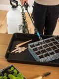 Close-up of a  woman using the Indoor-Outdoor Plant Sprayer with Tank 30' Coil Hose Wand to water a seed starting tray